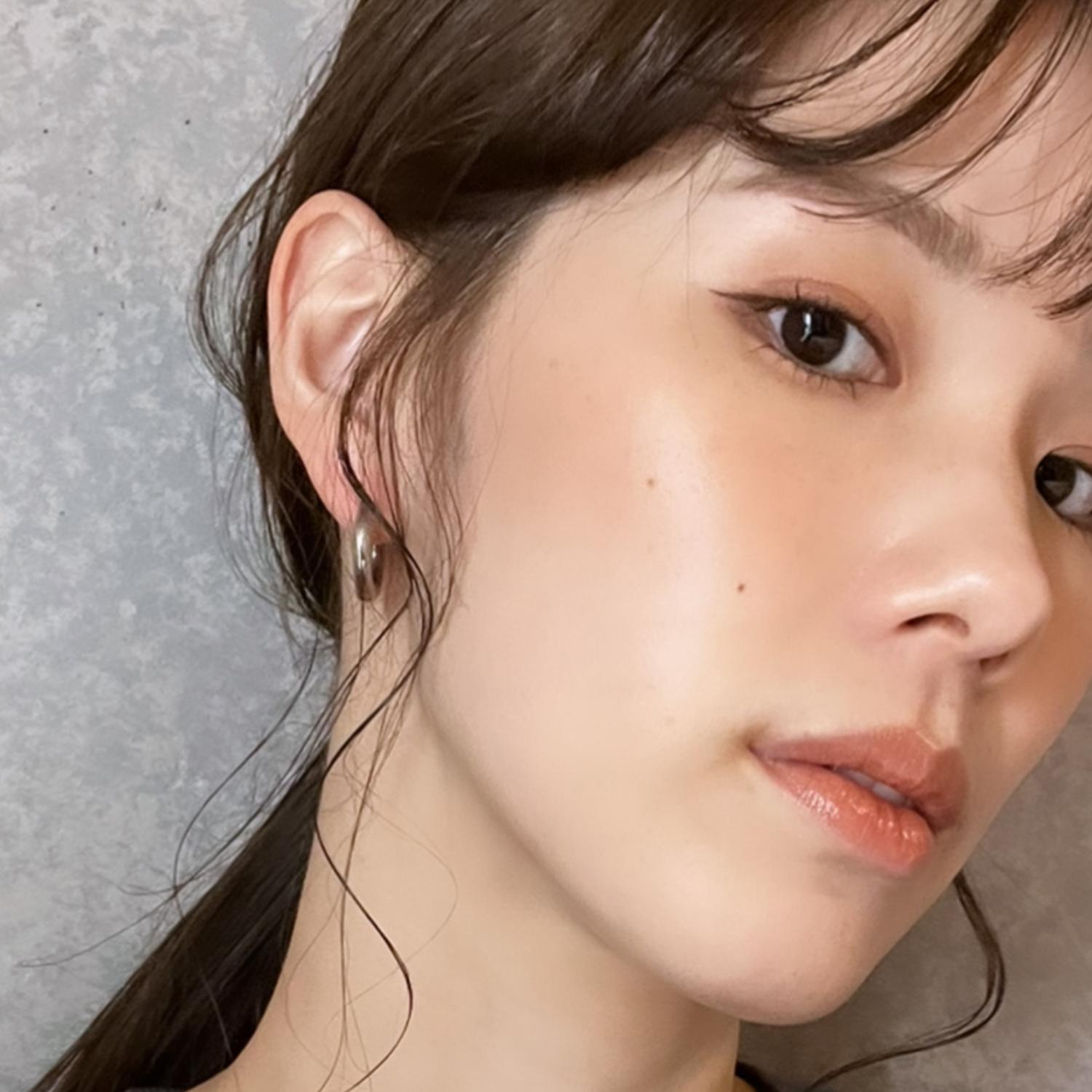 Close-up of a woman with long hair and hoop earrings, looking to the side. She has winged eyeliner and a neutral expression.