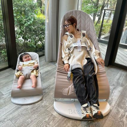 大人用と赤ちゃん用のベビーシートに座る女性と赤ちゃん。大きな窓から外の景色が見える。