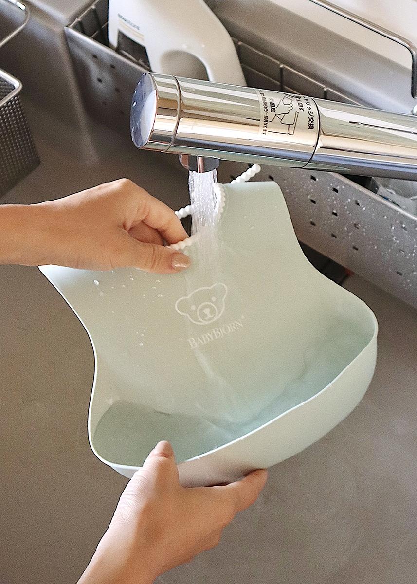 Hands rinsing a light blue bib under a running faucet in a kitchen sink.